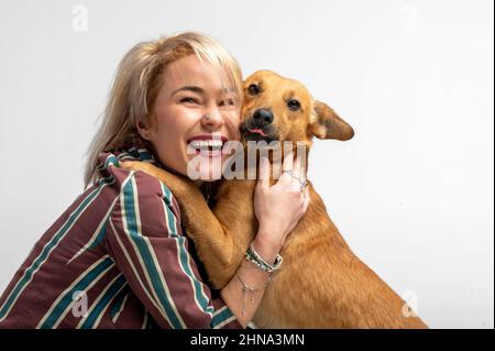 Eine niedliche junge Frau küsst und umarmt ihren Mischlingshund. Liebe zwischen Besitzer und Hund. Isoliert auf weißem Hintergrund. Studio-Porträt. Mädchen umarmt neue schöne Stockfoto