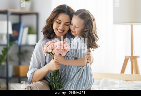 Guten Tag! Die Tochter gratuliert der Mutter und schenkt ihr Blumen. Mama und Mädchen lächeln und umarmen. Familienurlaub und Zweisamkeit. Stockfoto