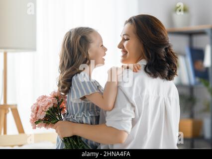 Guten Tag! Die Tochter gratuliert der Mutter und schenkt ihr Blumen. Mama und Mädchen lächeln und umarmen. Familienurlaub und Zweisamkeit. Stockfoto