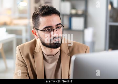 Nahaufnahme eines bärtigen Mannes in einer Brille, der während seiner Arbeit im Büro auf den Computermonitor schaute Stockfoto