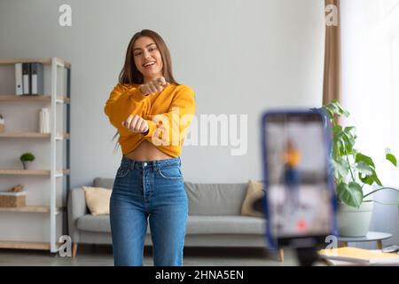 Junge kaukasische Influencerin, die Videos auf dem Smartphone aufzeichnet und zu Hause vor der Kamera tanzt Stockfoto
