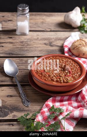 Hausgemachte Linsensuppe mit Zutaten auf Holzboden. Vertikales Format. Traditionelles spanisches Gericht. Stockfoto