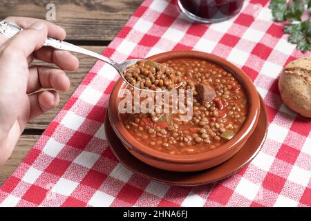 Die Hand des Mannes nimmt einen Löffel Linsen auf dem Holztisch auf. Stockfoto