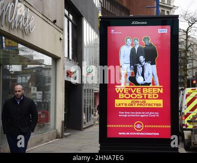 Die Menschen laufen an einem elektronischen Schild der Regierung NHS und HM vorbei, das „Wir wurden aufgestockt“ wurde, um für den Auffrischungsimpfstoff zur Bekämpfung von Covid-19 in Manchester, Greater Manchester, England, Großbritannien, zu werben. Die Zahl der Covid-19-, Coronavirus- oder Corona-Infektionen im Großraum Manchester sinkt weiter. In der Woche bis zum 8th. Februar 2022 wurden in der Region 12.364 Personen positiv getestet, was einem Rückgang um 35 Prozent gegenüber der Vorwoche entspricht. Stockfoto