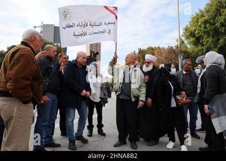 Am 15. februar 2022 protestieren Eltern libanesischer Studenten aus dem Ausland vor dem Botschaftskomplex in der Nähe des Platzes Riad Al Solh in Beirut, Libanon. Der Mann mit der blauen Jacke, Nemer, ist Vater von zwei Studenten an einer ukrainischen Universität; die verschleierte Frau in Stiefeln in der Mitte des Fotos, Fatima, hat eine Tochter, die in Weißrussland studiert; der kahle Mann, der das Banner trägt, Ahmed, ist Vater eines Studenten in der Ukraine. Die Vereinigung der Familien von Studenten an ausländischen Universitäten prangert die Not an, die ihre Kinder erleben, da libanesische Banken sie daran hindern, Gelder ins Ausland zu überweisen. Si Stockfoto