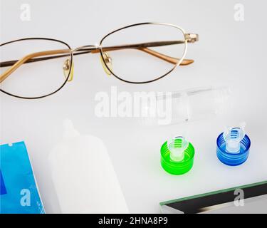 Kontaktlinsen-Set mit Linsen, Behälter, Brille und Augentropfen auf einem weißen Tisch. Das Konzept der richtigen Verwendung von Kontakt- und Nachtlinsen und deren Pflege. Stockfoto