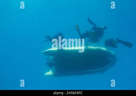 Ein Blick unter Wasser auf Taucher (MR), die von einem aufblasbaren Schlauchboot abgeholt werden, Philippinen. Stockfoto