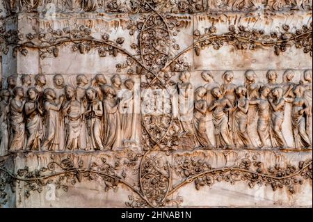 Heilige und Engel eingerahmt von blühenden Weinreben aus dem 1300 letzten Jüngsten Jüngsten Jüngsten Jüngsten Jüngsten Jüngsten Marmor an der Westfront der Kathedrale von Orvieto, Umbrien, Italien. Diese Skulptur wird Lorenzo Maitani (ca. 1275–1330) zugeschrieben, der die spätgotische Fassade der Kathedrale entwarf. Maitani soll als Bildhauer direkt auf zwei Tafeln eingegangen sein, die zwei der vier unteren Pilaster der Fassade bedecken: Eine Maitani-Platte zeigt Szenen aus dem Jüngsten Gericht, einschließlich der Szene in diesem Bild. Stockfoto