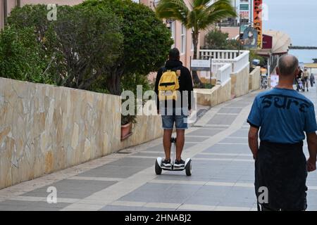 Ein Mann auf einem Segway, der auf einer gepflasterten Straße entlang zur Küste im Zentrum von Costa Adeje, Teneriffa, Spanien, fährt Stockfoto