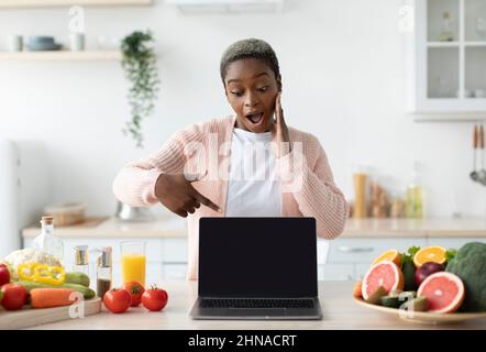 Schockiert tausendjährige afroamerikanische Dame mit offenem Mund zeigen Finger auf Laptop mit leerem Bildschirm Stockfoto