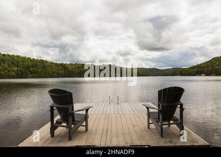 Schwimmende Anlegestelle mit zwei Adirondack-Stühlen mit Blick auf den See im Sommer. Stockfoto