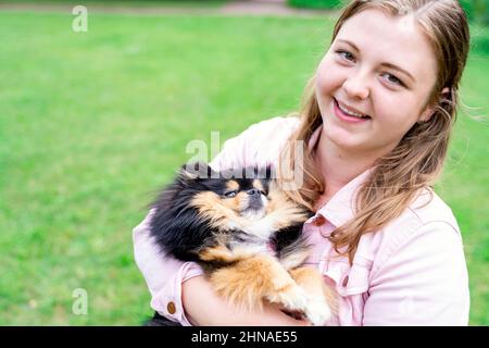 Porträt einer jungen blonden Frau umarmt ihren Hund Spitz Pommeranian draußen im Park Stockfoto