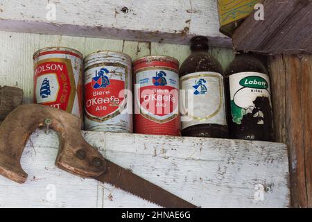 Alte Säge, Bierdosen und Flaschen im Regal in der alten rustikalen Holzdiele-Hütte, Quebec. Stockfoto