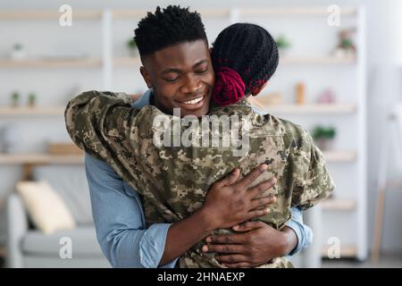Glückliche schwarze Familie militärische Frau und Mann umarmt zu Hause Stockfoto