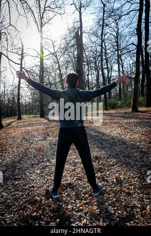Der Läufer streckt sich im Wald. Mann von hinten mit offenen Armen gesehen. Stockfoto