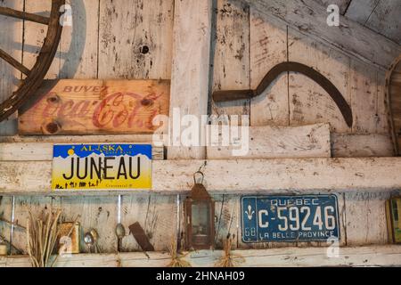 Antikes Coca Cola Holzschild, Öllampe, Sichel, Nummernschilder und Löffel an der Wand in der alten rustikalen Holzplankenhütte. Stockfoto