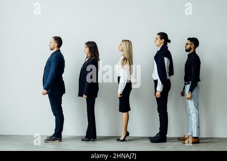 Langen Reihe von vielfältigen professionellen Geschäftsleute stehen in einer Warteschlange im Profil isoliert auf weiss Stockfoto