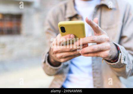 Schneiden Sie unkenntlich männliche touristische Textnachrichten auf einem modernen Mobiltelefon, während Sie auf der Straße mit Gebäuden in der Stadt vor verschwommenem Hintergrund stehen Stockfoto