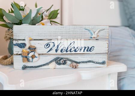 Hölzerne Willkommensschild an der Rezeption im Hotel, antike rustikale Tafel, Willkommensteller aus Holz mit schöner maritimer Dekoration. Sommer Meer Stockfoto