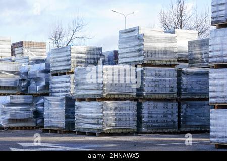 Ein Stapel neuer Pflasterplatten auf einer Holzpalette, die in durchsichtige Kunststoffverpackung in einem Lagerhof eingewickelt ist Stockfoto