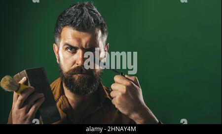 Bärtiger Mann mit Rasiermesser, Holzschatulle, Rasierpinsel in den Händen. Werbung für Barbershop Stockfoto