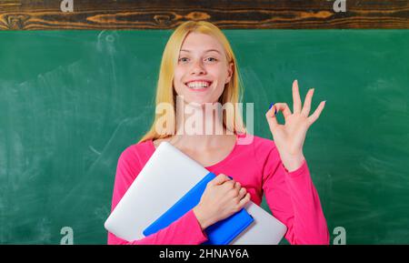 Lächelnder Schüler im Klassenzimmer zeigt okay. Lehrerin mit Notizbuch machen ok Zeichen mit Fingern. Stockfoto