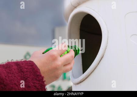 Frau oder weibliche Hand werfen leere grüne Glasflasche in Papierkorb Abfallbehälter. Natur Liebe, Abfallsortierung, Recycling, Pflege Konzept Idee. Stockfoto