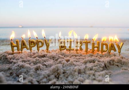 Kerzen Gold Buchstaben Happy Birthday Brennen auf Hintergrund von verschwommenen Meereswellen Stockfoto