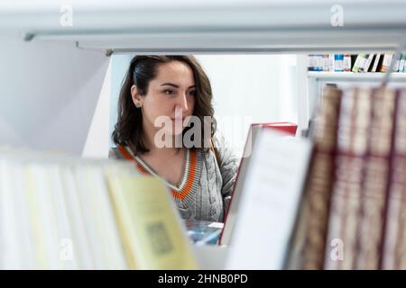 Junge kaukasische Frau, die Bücher in einer Bibliothek ansieht. Selektiver Fokus. Platz für Text. Stockfoto