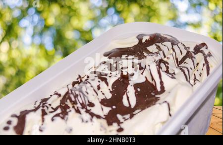 Leckeres Eis mit Schokolade in Plastikbecher auf Holztisch Stockfoto