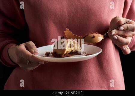 Knusprige Tarte mit zarter Schokoladenmousse und gesalzenem Karamell. In den Händen der Frauen. Morgens Kuchen zum Frühstück. Stockfoto