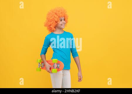 Fröhliches egoistisches Kindermädchen in lockiger Perücke hält Penny Board, Hipster Stockfoto