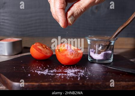 Koch salzen eine halbierte Tomate auf einem Holzschneidebrett Stockfoto