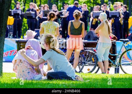 Mädchen auf dem Rasen lauschen einer Blaskapelle im Park. Minsk (Weißrussland). 9.Mai 2018 Stockfoto