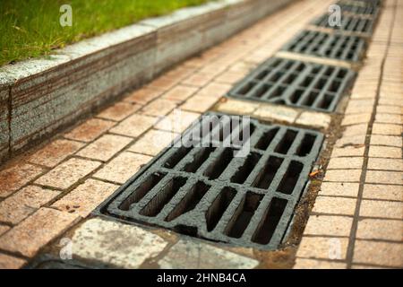 Sturmabfluss für die Wasserableitung. Details der städtischen Kommunikation. Luken des Kanals. Rost auf der Straße. Abfluss für Regenwasser. Stockfoto