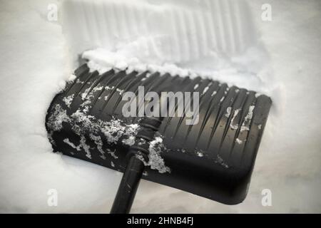 Schaufel im Schnee. Schwarze Schaufel zum Schneeräumen. Schneeverwehungen auf der Straße werden gereinigt. Stockfoto