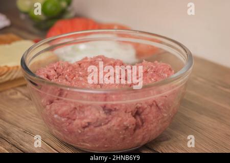 Glasschüssel mit Hackfleisch aus rohem Rindfleisch oder Schweinefleisch auf einem Holztisch im Komfort von zu Hause Stockfoto