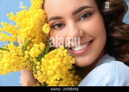 Schöne junge Frau mit Bouquet von Mimosenblüten auf blauem Hintergrund, Nahaufnahme Stockfoto