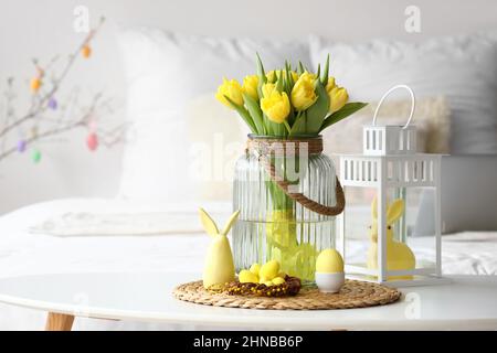 Vase mit Tulpen, Nest mit Ostereiern und Dekor auf dem Tisch in hellem Raum Stockfoto