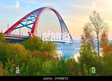 Bugrinsky Brücke im goldenen Herbst. Gewölbte Automobilbrücke am Ufer des ob, zwischen den Baumkronen. Nowosibirsk, Sibirien, Russland, 2021 Stockfoto