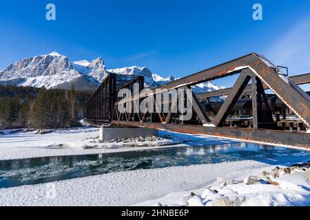 Canadian Rockies wunderschöne Landschaft im Winter. Schneebedeckte Bergkette Reflexion auf Bow River. Canmore Engine Bridge Banff National Park. Stockfoto