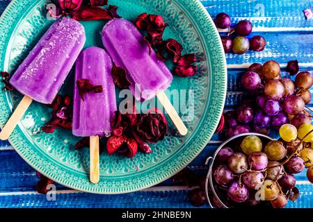 Traubeneis im Lollipop-Stil auf einem Stock auf einem Vintage-Teller auf einem hellblauen Holztisch. Konzept der natürlichen und gesunden Ernährung. Copyspace. Stockfoto