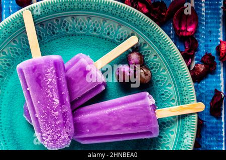 Traubeneis im Lollipop-Stil auf einem Stock auf einem Vintage-Teller auf einem hellblauen Holztisch. Konzept der natürlichen und gesunden Ernährung. Stockfoto