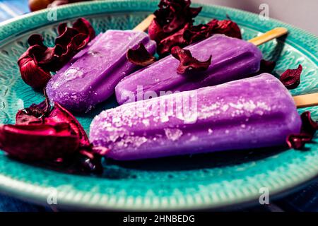 Traubeneis im Lollipop-Stil auf einem Stock auf einem Vintage-Teller auf einem hellblauen Holztisch. Konzept der natürlichen und gesunden Ernährung. . Stockfoto