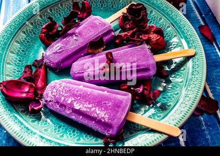 Ein Traubeneis im Lollipop-Stil auf einem Stock auf einem Vintage-Teller auf einem hellblauen Holztisch. Konzept der natürlichen und gesunden Ernährung. Stockfoto
