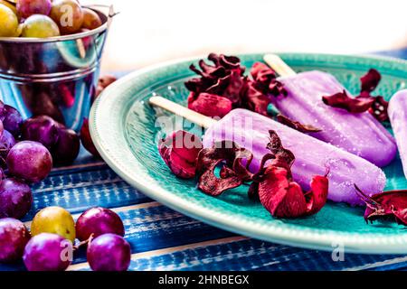 Ein Traubeneis im Lollipop-Stil auf einem Stock auf einem Vintage-Teller auf einem hellblauen Holztisch. Konzept der natürlichen und gesunden Ernährung. Stockfoto