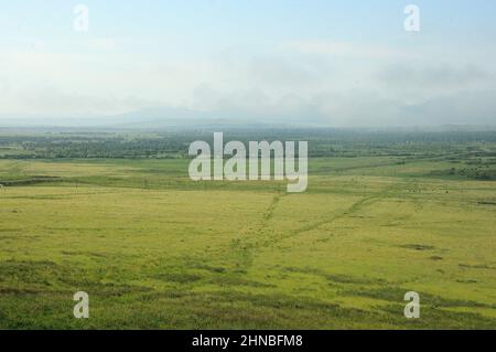 Endlose Steppe und ein großer Wald am Fuße einer Bergkette mit Gipfeln in den Wolken. Chakassien, Sibirien, Russland. Stockfoto