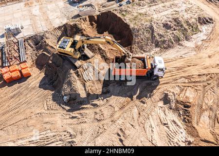 Lader Bagger belädt den Boden im LKW auf der Baustelle. Luftaufnahme von oben. Stockfoto