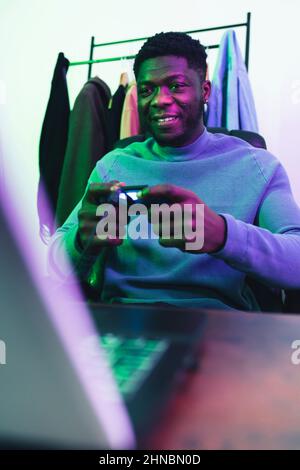 Glücklicher afroamerikanischer Mann, der auf dem Computerspielfeld spielt - mittlerer Schuss. Hochwertige Fotos Stockfoto