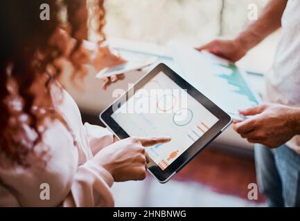 So sollte der Fortschritt aussehen. Aufnahme von zwei Händen, die nicht mehr erkennbar sind, die auf einem Tablet arbeiten und sich die Geschäftscharts im angucken Stockfoto